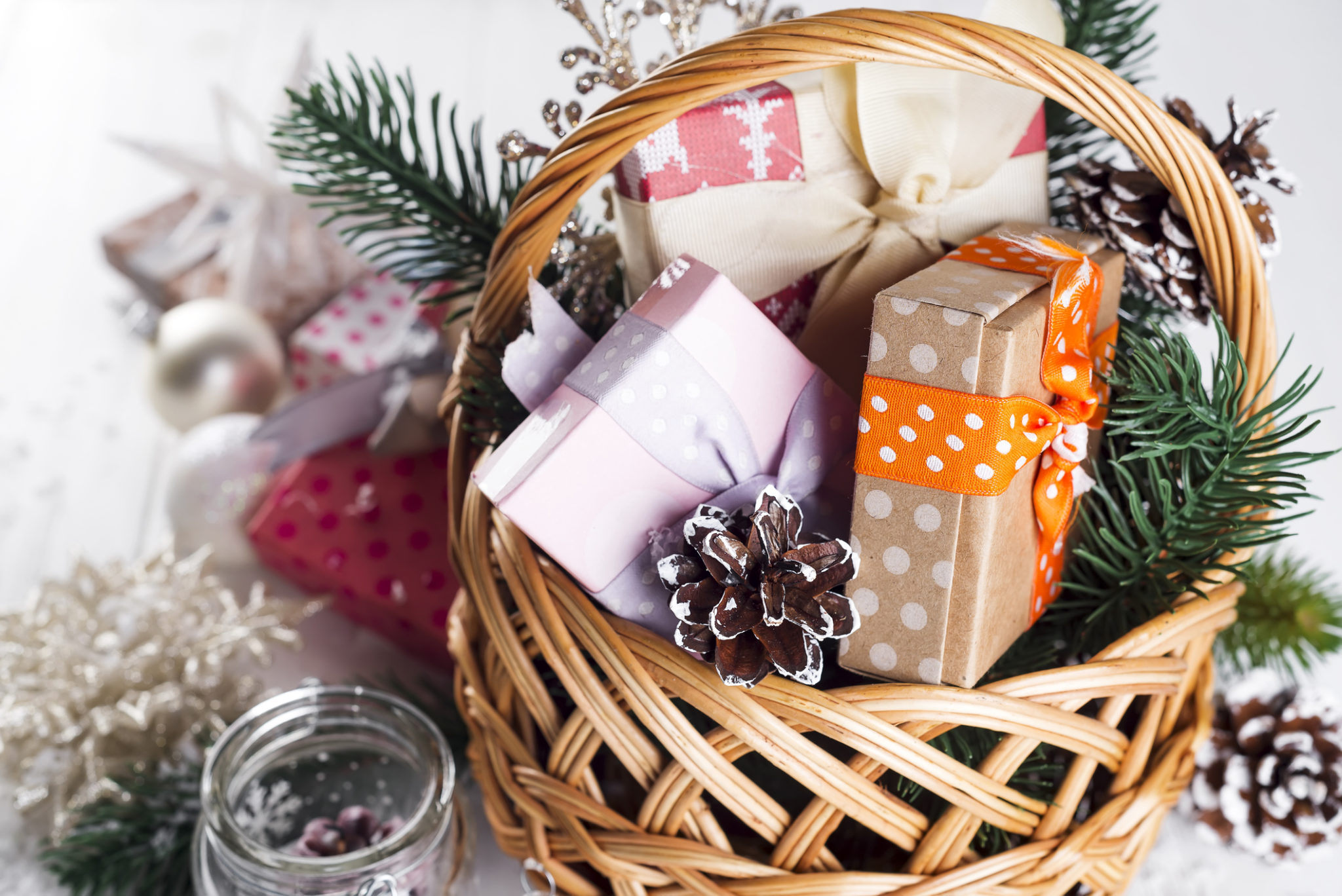 Christmas Gifts in a basket with Candle, balls, pine cones, snowflakes on white Wooden Background.